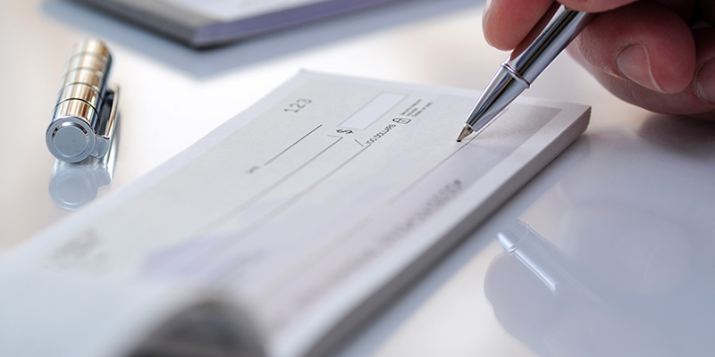 close up of check on a desk with someone holding a pen to sign the check