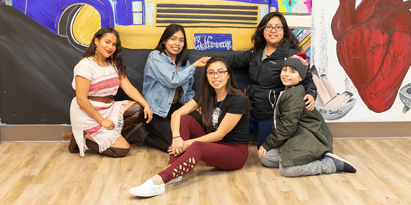 a group of women and a child pose in front of a mural at Centro Hispano of Dane County