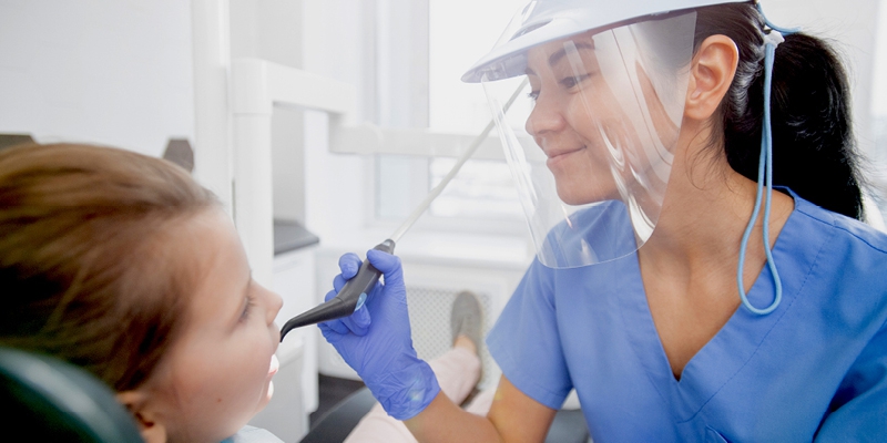 dental hygienist smiling and cleaning a child's teeth